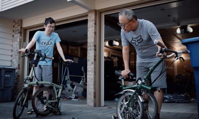 Two people in t-shirt and shorts stand with folding cycles.